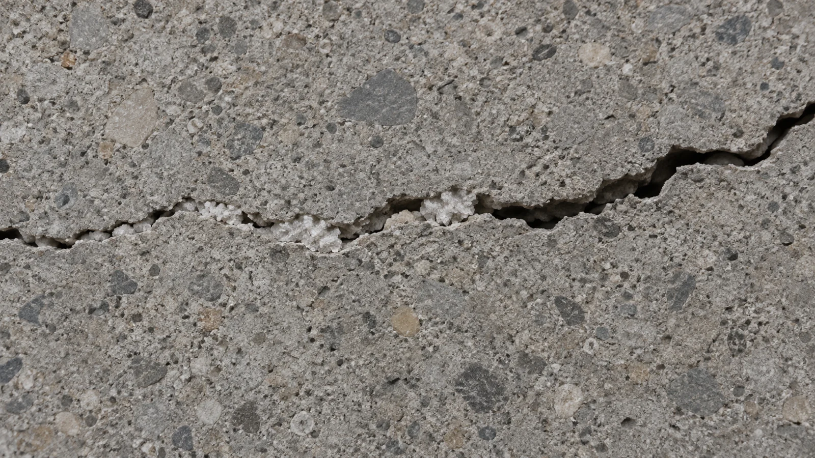 Conceptual concrete cross-section with partial mineral infill in a narrow crack, leaving one section open.